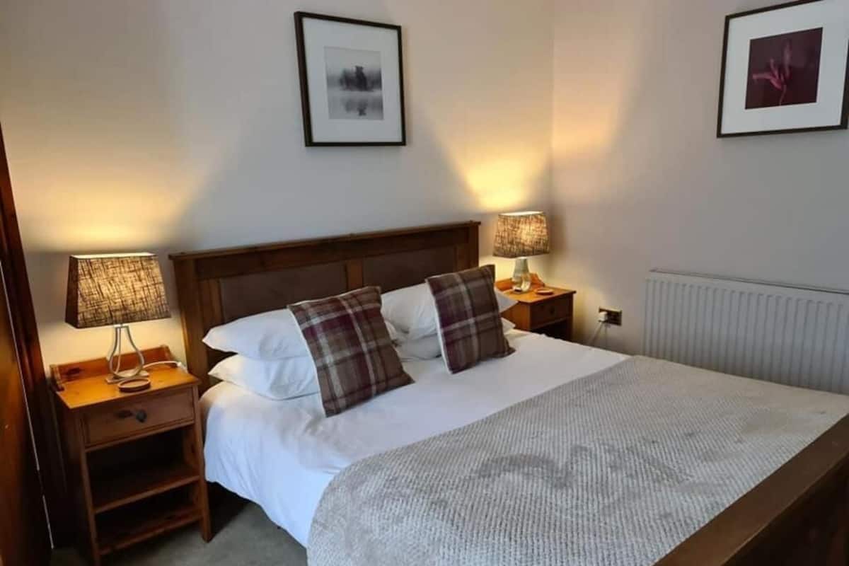A neatly made bed with a headboard, two bedside tables with lamps, and framed pictures on the wall.