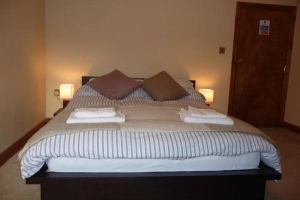 A neatly made bed with striped bedding, two pillows, and folded towels. There are two bedside lamps, a wooden door, and a small sign on the door.