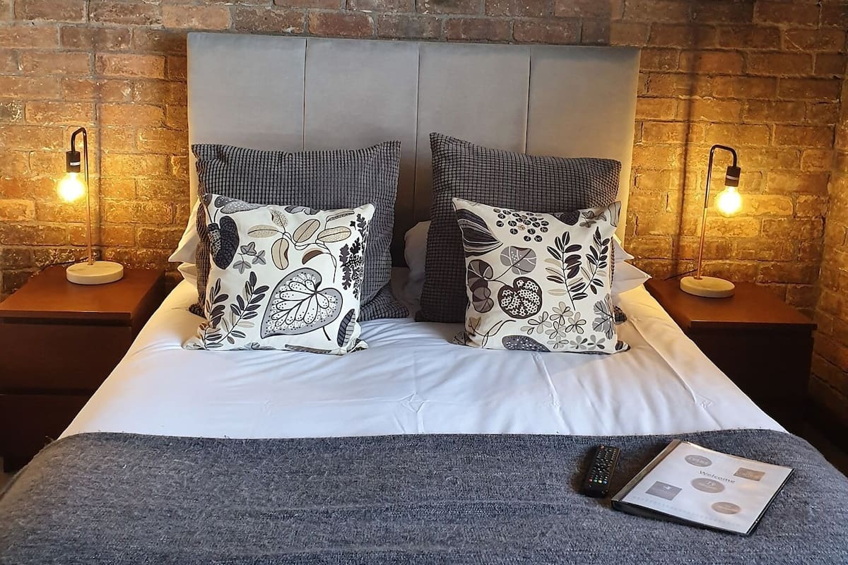 A bed with two pillows, a remote control, and a welcome booklet on a grey textured bedspread.