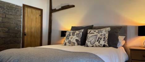 Ein Schlafzimmer mit Bett, Kissen, Nachttisch, einem Holzkopfende, einer Steinwand und einer Holztür.