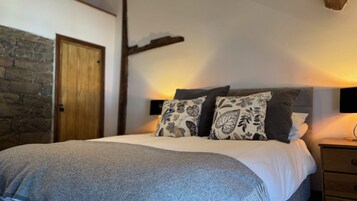 Un dormitorio con una cama, almohadas, una mesita de noche, un cabecero de madera, una pared de piedra y una puerta de madera.