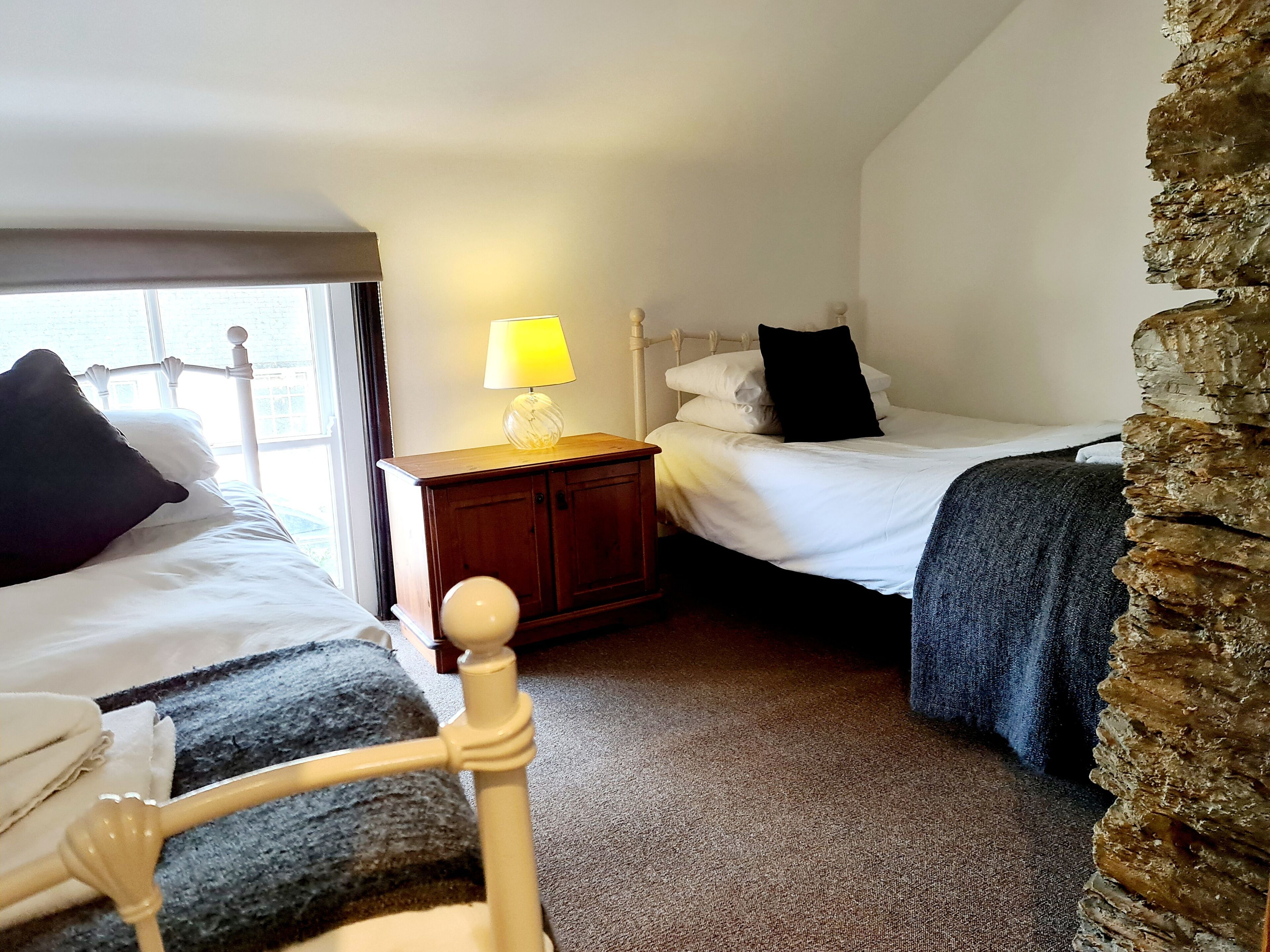 Een kamer met twee bedden, een nachtkastje met een lamp en een stenen muur.