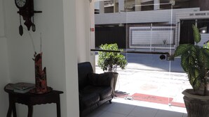 A living room with a sofa, a table with a clock, a potted plant, and a view of the street outside. - Studio 51 (Jaboatão dos Guararapes)