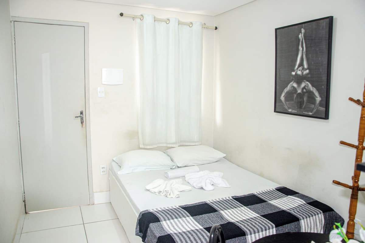 Cama bem arrumada com manta xadrez, travesseiro branco e toalhas dobradas.