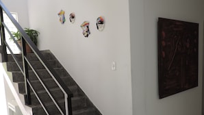 A staircase with a metal railing leading to a landing. On the landing, there are several decorative items on the wall, including a framed artwork and a potted plant. - Studio 51 (Jaboatão dos Guararapes)