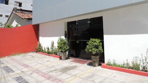A modern building with a white facade, a red wall, and a tiled entrance area with potted plants. - Studio 51 (Jaboatão dos Guararapes)