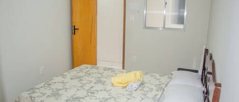 A bedroom with a bed, a window with blinds, a door, and a thermostat on the wall.