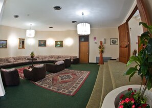 A spacious living room with a sectional sofa, multiple armchairs, a patterned rug, and a large plant.