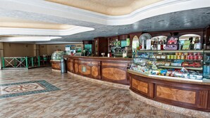 A spacious lobby with a curved reception desk, a coffee machine, and a display case filled with snacks. - Hotel Villaggio Club ALTALIA (Brancaleone)