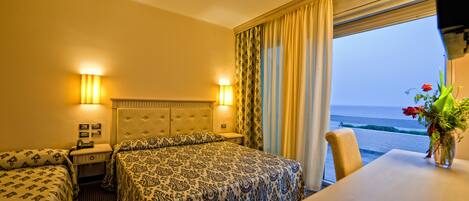 A hotel room with a bed, a bedside table, a chair, a window with curtains, and a view of the sea.