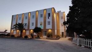 Ein mehrstöckiges Hotel mit modernem Design, das einen zentralen Innenhof mit Palmen und einem weißen Zaun umfasst.