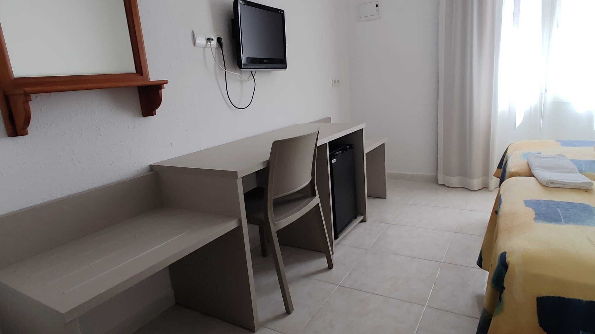 Hotellihuone, jossa on työpöytä, tuoli, televisio ja sänky, jossa on peitto.