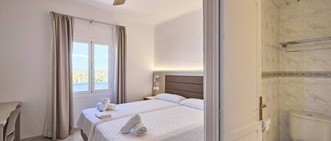 A hotel room with a bed, a desk, a chair, a bathroom, and a ceiling fan.