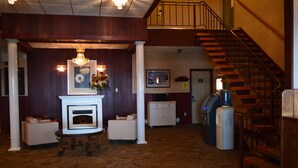 A lobby with a fireplace, seating area, staircase, and a water dispenser. - Hotel Port Aux Basques (Channel-Port aux Basques)