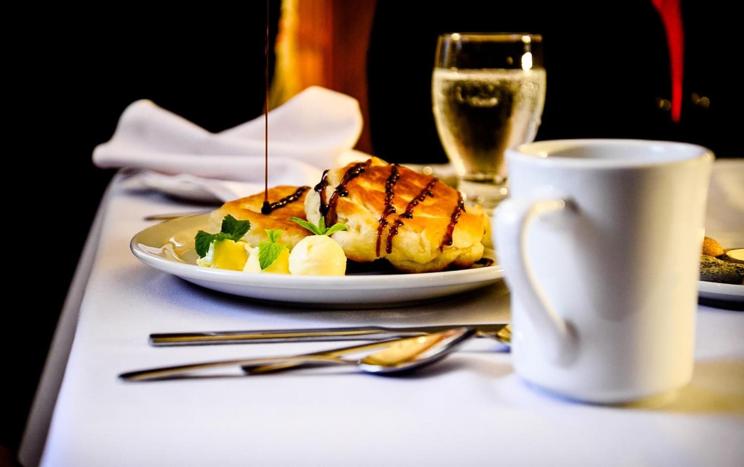 A dessert plate with a pastry, a glass of white wine, and a white mug on a table.