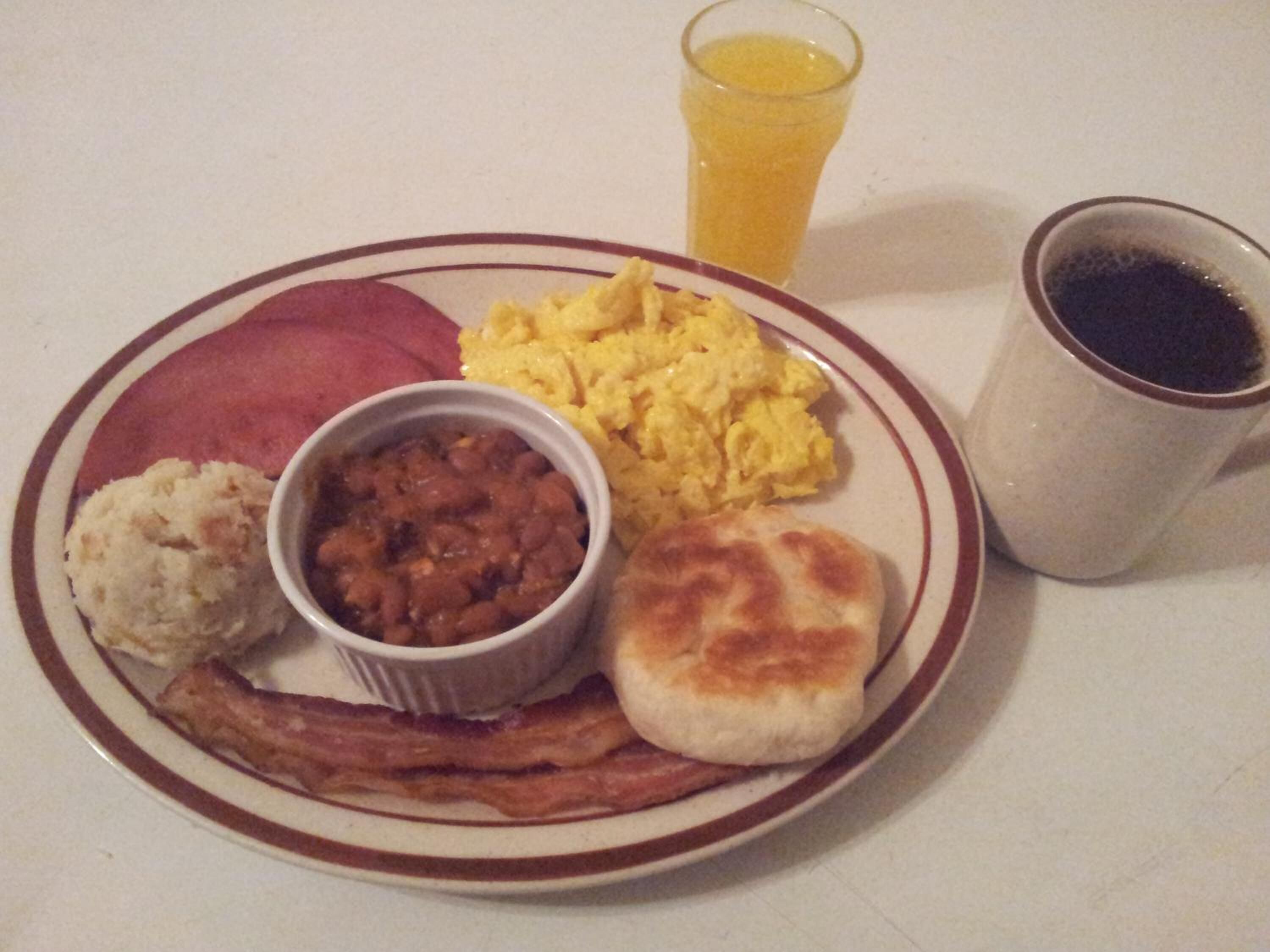 A plate with scrambled eggs, beans, sausage, and a biscuit.