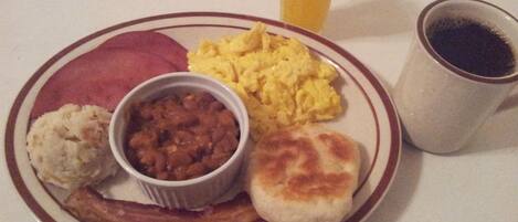 Un plato con huevos revueltos, frijoles, salchicha y un bizcocho.