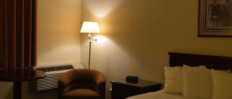 Una habitación de hotel con una cama, una silla, una mesita de noche, una lámpara y un cuadro en la pared.