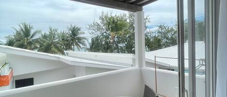 A balcony with wicker furniture, a glass door, and a view of palm trees and a cloudy sky.