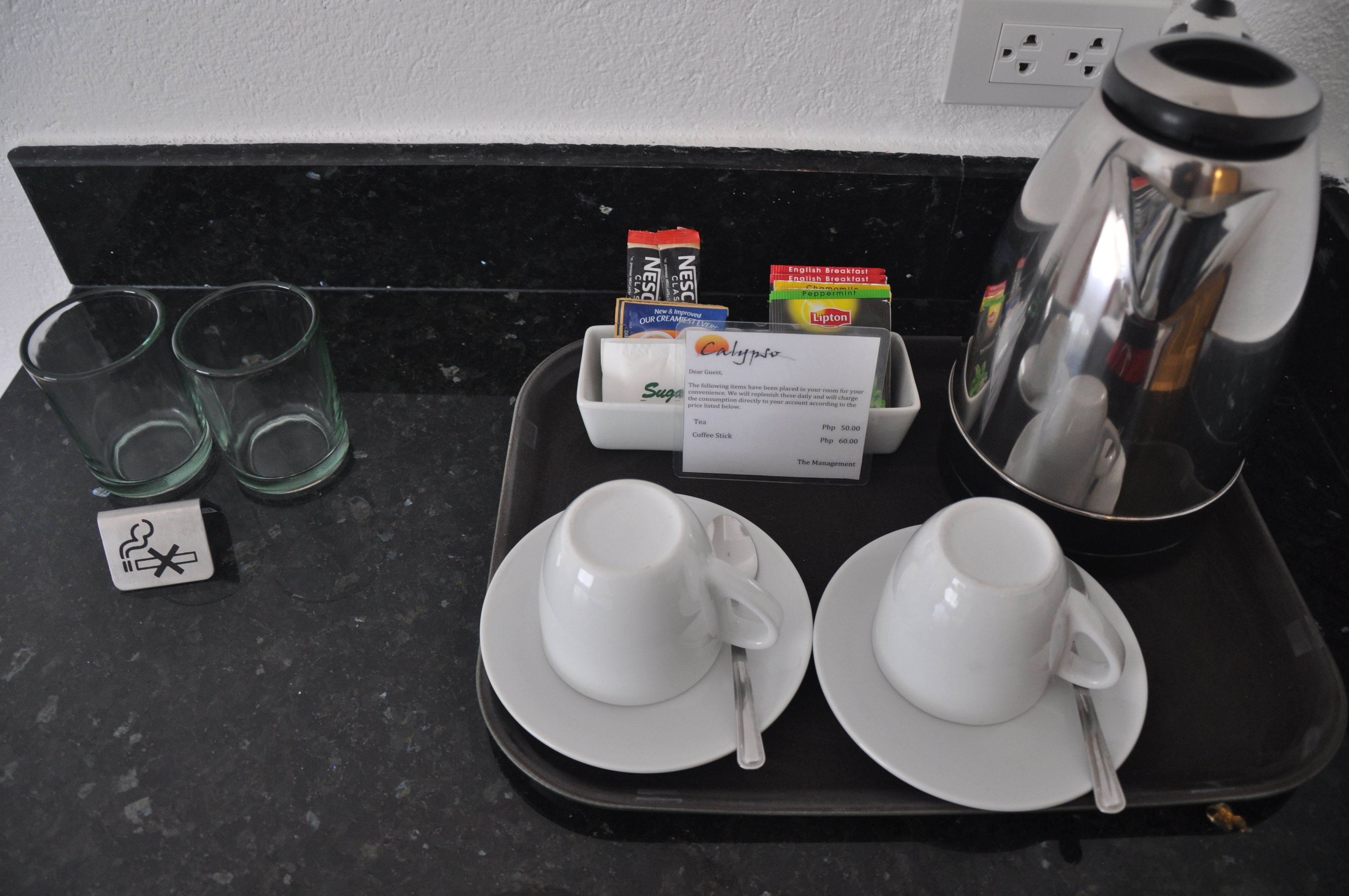 A tray with two white cups and saucers, a coffee pot, and a menu card on a black countertop.