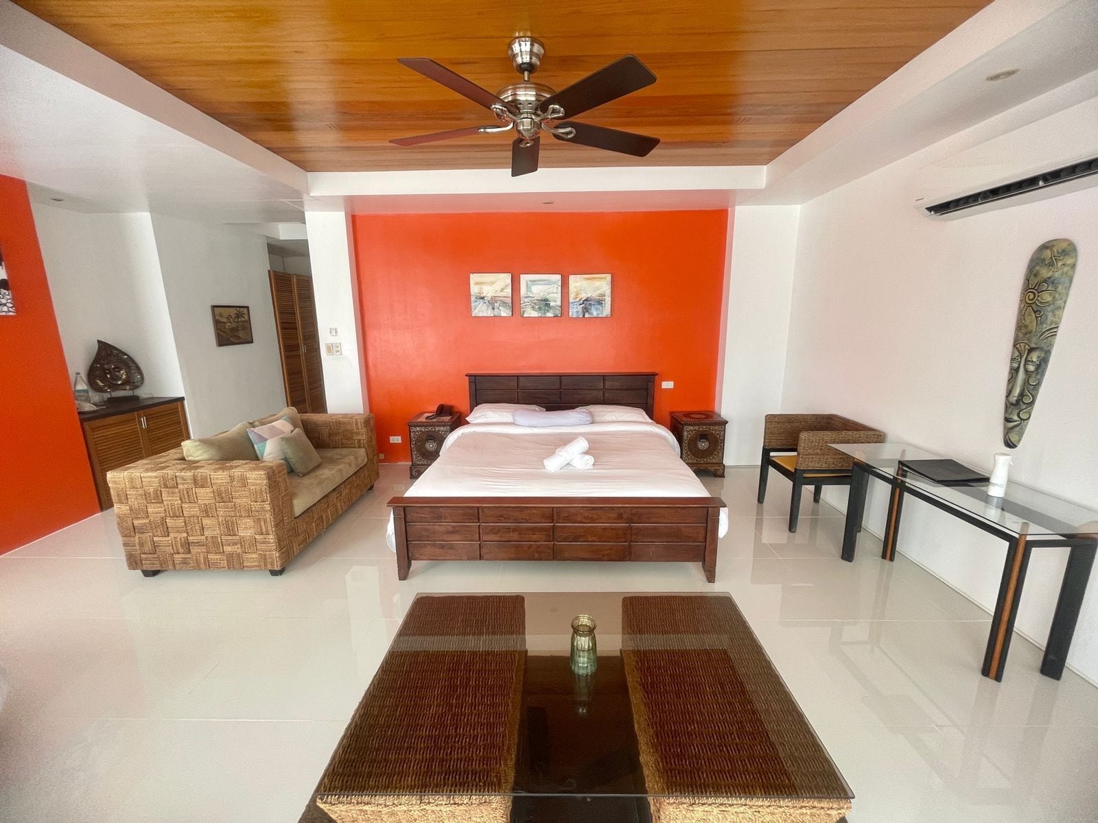Un dormitorio espacioso con una cama grande, un ventilador de techo de madera y una pared de acento naranja brillante.