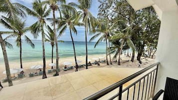 A balcony with a view of a beach, palm trees, and a clear sky.