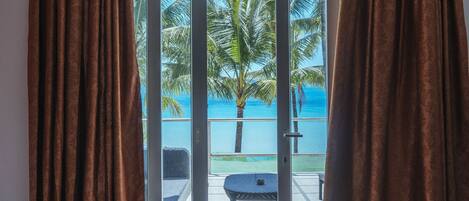 A bedroom with a large sliding glass door leading to a balcony with a view of palm trees and the ocean.