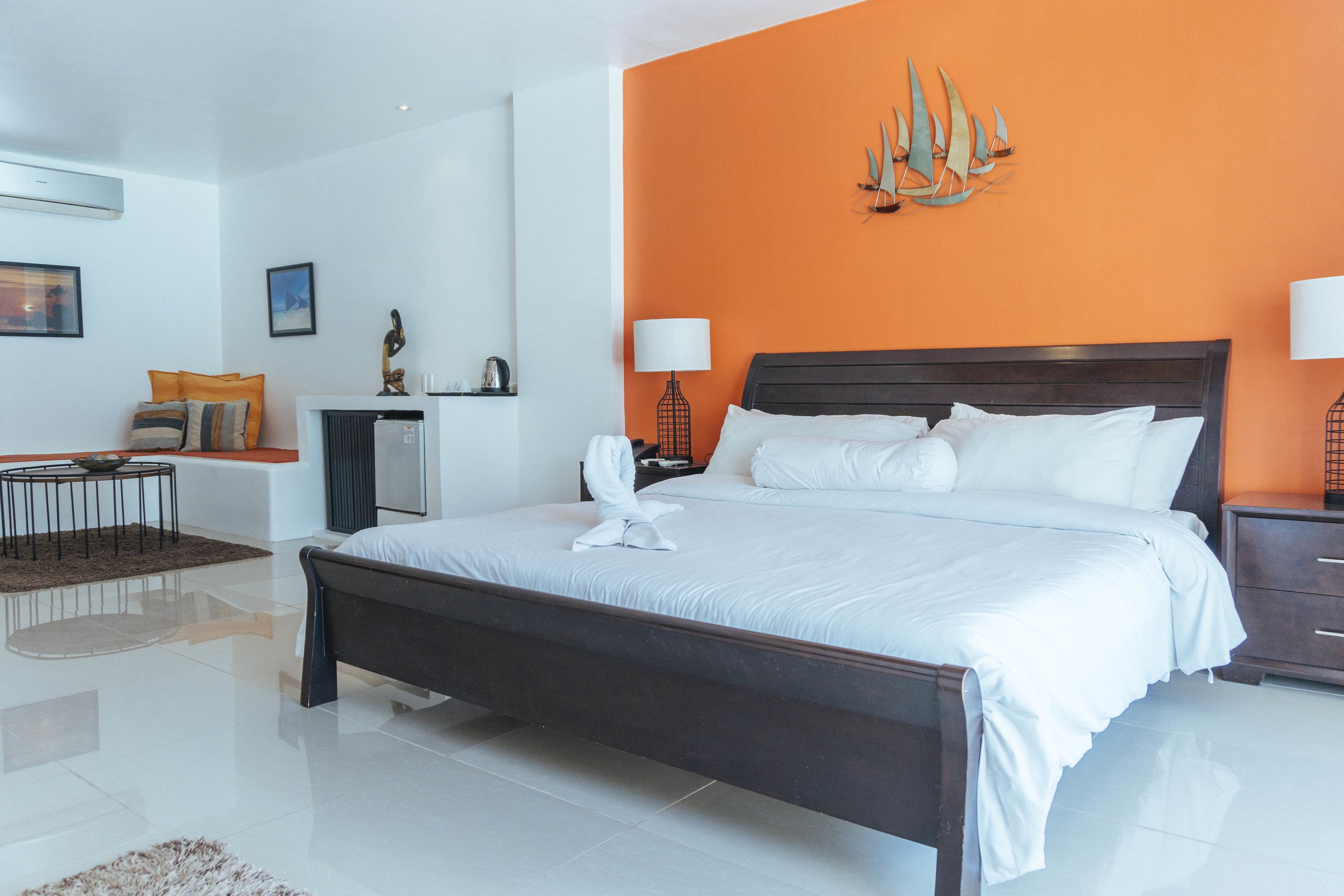 Une chambre d’hôtel moderne avec un grand lit, un petit bureau et un mur d’accent de couleur orange vif.