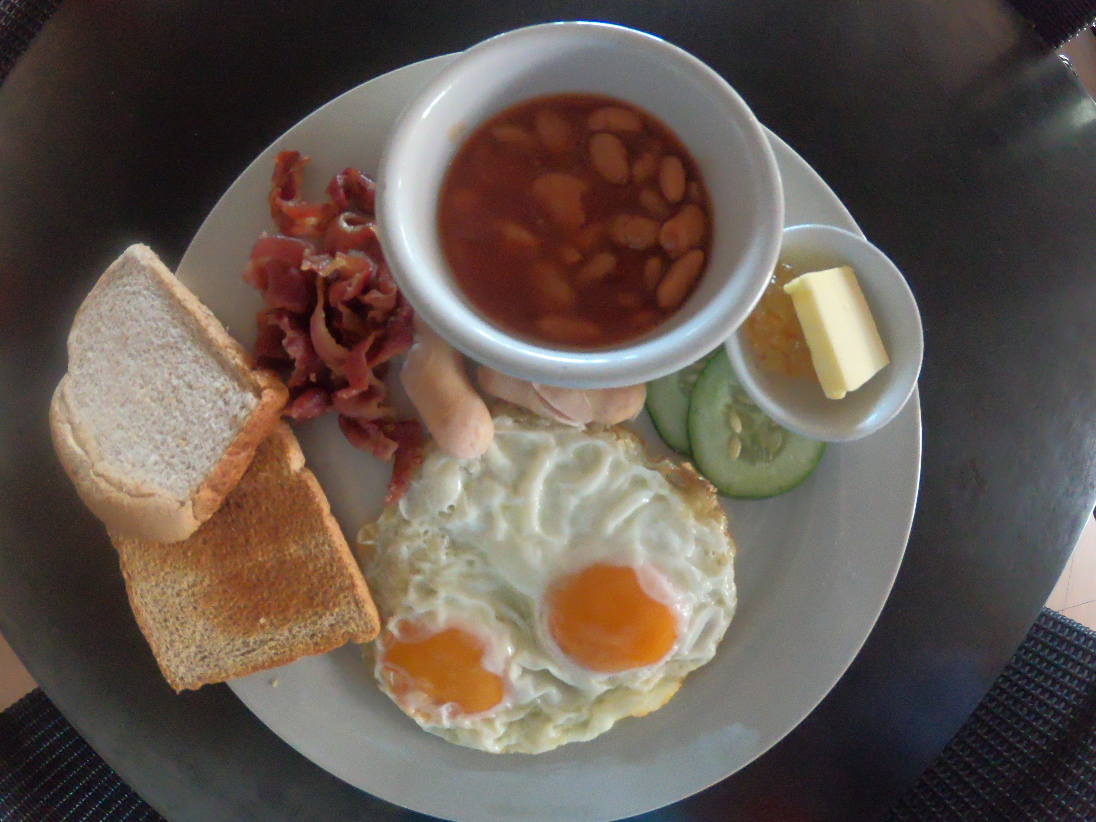 Ein Teller mit Toast, Spiegeleiern, Bohnen, Speck und einer kleinen Butterportion.