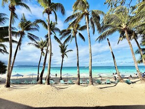Een strand met palmbomen, helderblauw water en mensen die zwemmen.