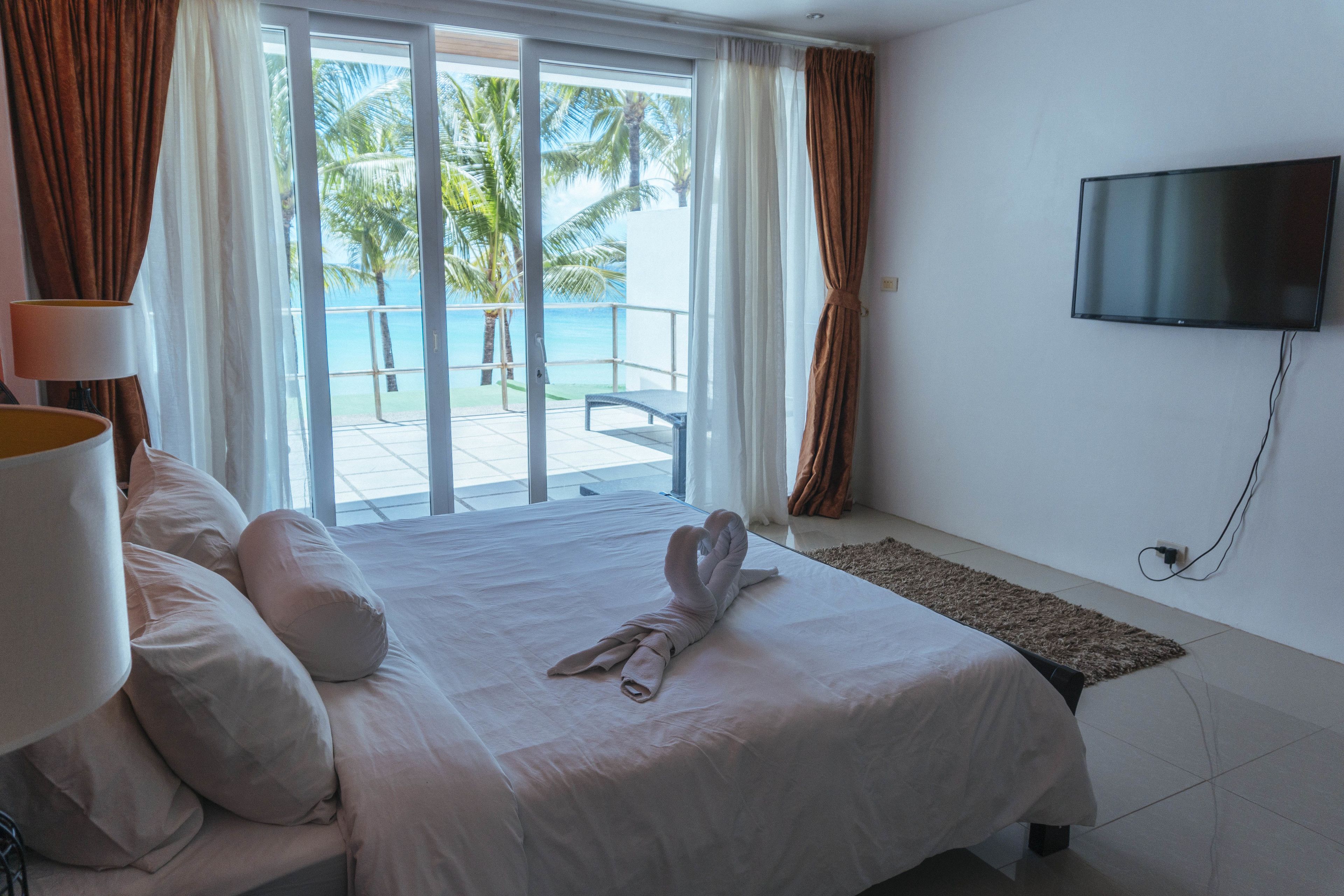 A hotel room with a bed, a TV, a view of the ocean, and a balcony with a palm tree.