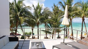 A balcony with a sofa, a table, and lounge chairs overlooking a beach with palm trees and the ocean. - Calypso Beach & Dive Resort (Boracay Island)