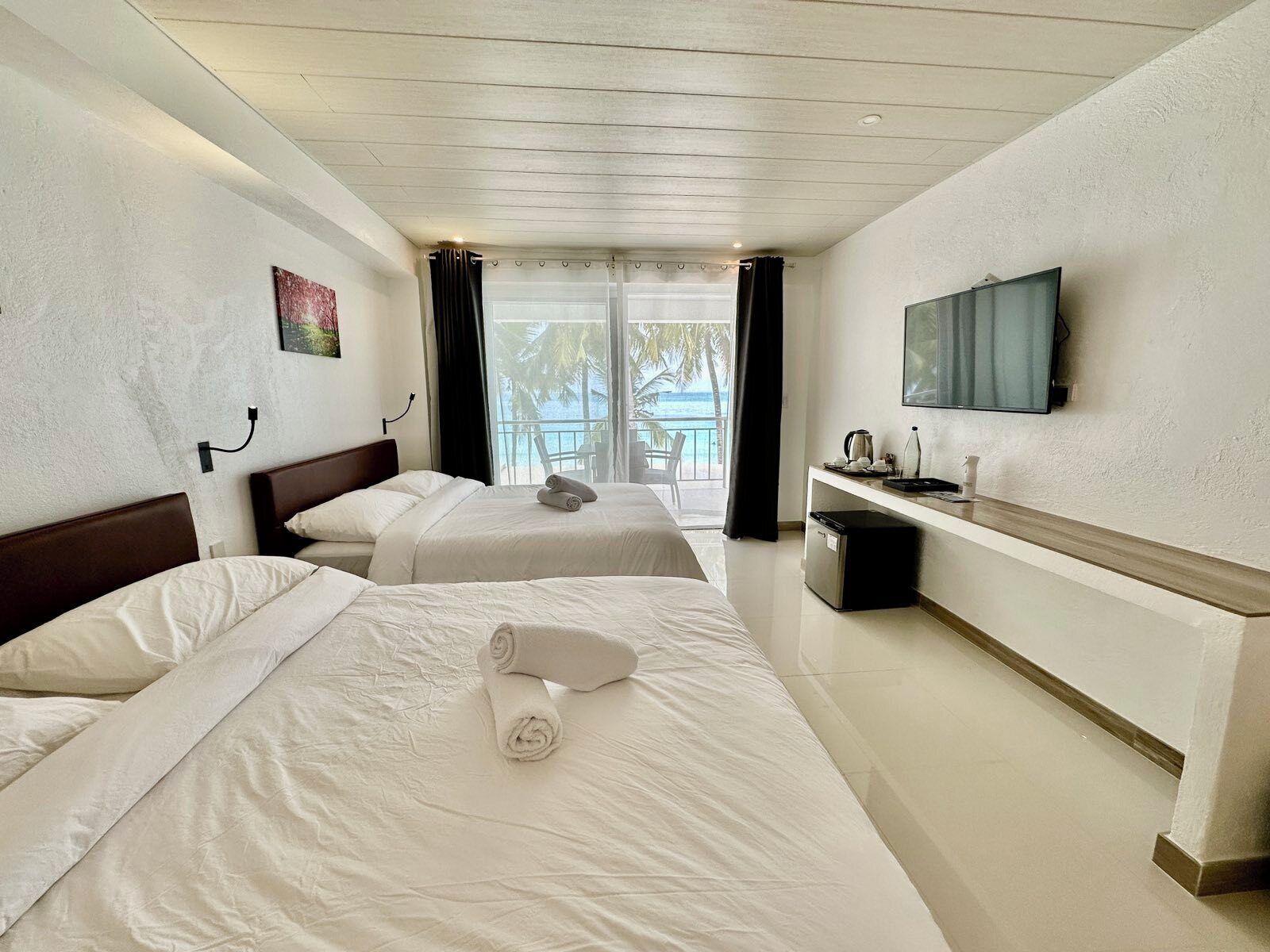 Quarto de hotel com duas camas, televisão, escrivaninha com cafeteira e vista para o oceano.