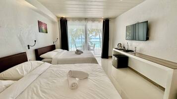 A hotel room with two beds, a TV, a desk with a coffee maker, and a view of the ocean.