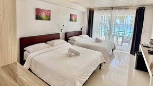 A hotel room with two beds, a wooden desk, a balcony with a view, and artwork on the walls. - Calypso Beach & Dive Resort (Boracay Island)