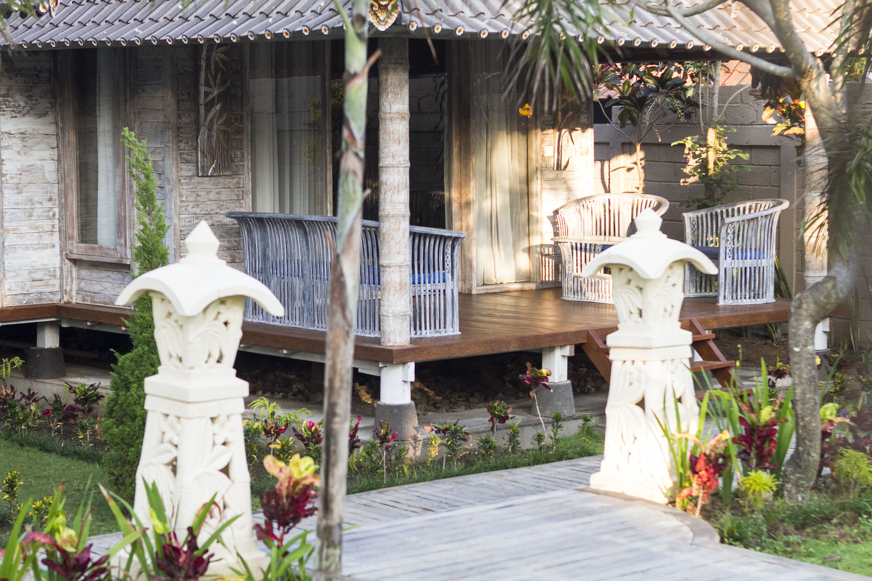 A wooden house with a porch, white railings, and a garden with various plants.