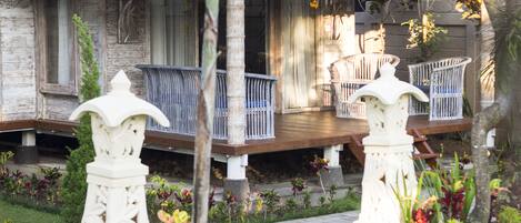 A wooden house with a porch, white railings, and a garden with various plants.