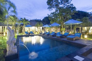 A pool area with lounge chairs and umbrellas, surrounded by palm trees and a statue.