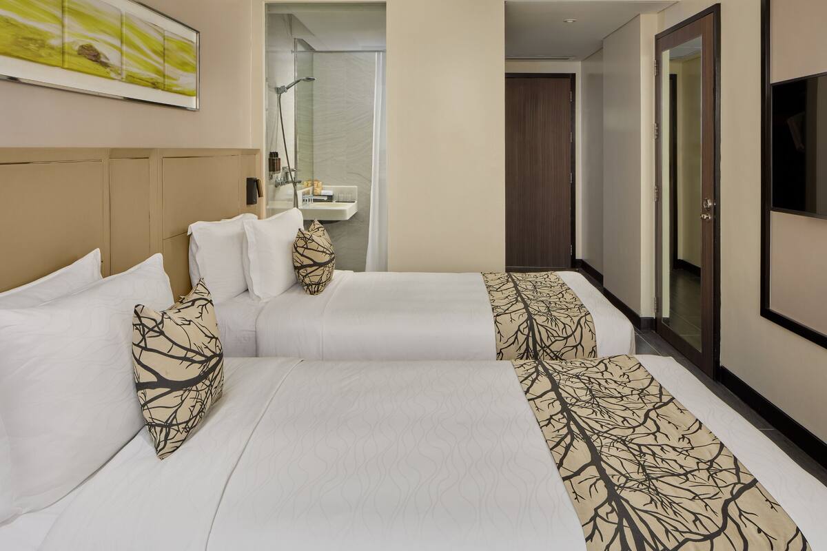 A hotel room with two beds, a bathroom, and a TV.