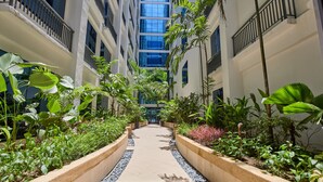 A corridor with a central pathway flanked by planters with various plants and a building with multiple floors in the background.