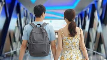 A couple walking through a corridor with a modern design, featuring blue lighting and a glass ceiling.