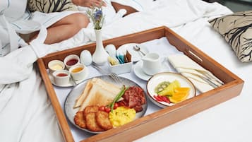 Ein Frühstücksbrett mit Toast, Eiern, Speck und Obst auf einem Bett.