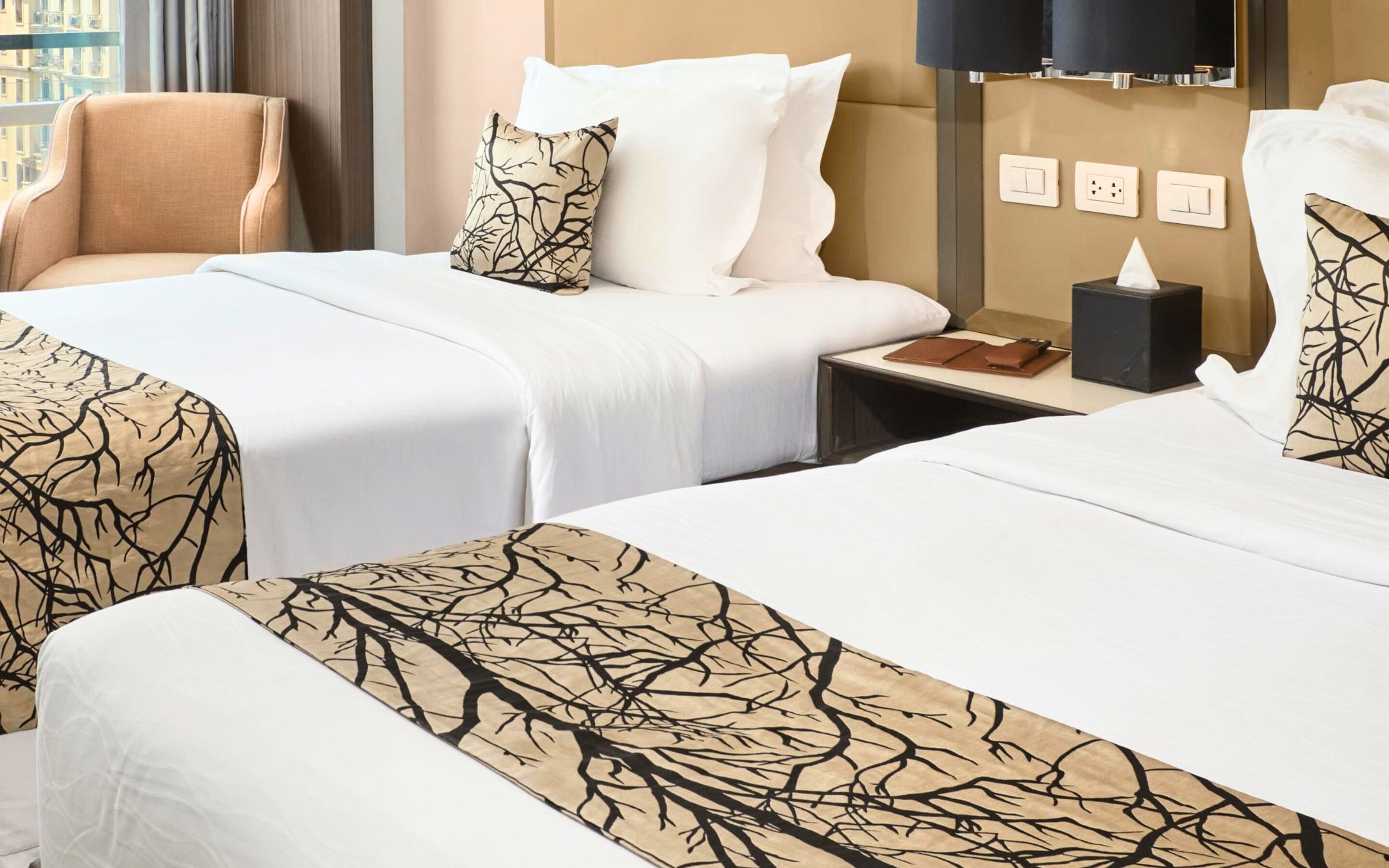 Habitación de hotel con dos camas, una silla, una mesita de noche y una lámpara de pared.