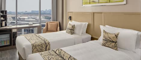 A hotel room with two beds, a desk with a computer, a mirror, and a view of the cityscape.