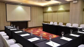 A conference room with a long table, white chairs, and a projector screen.