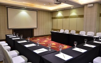 A conference room with a long table, white chairs, and a projector screen.