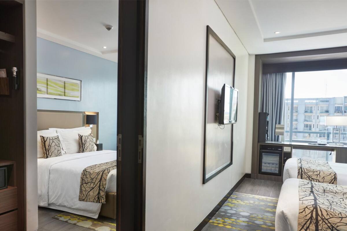 A hotel room with a bed, a desk, a TV, and a large window with a city view.