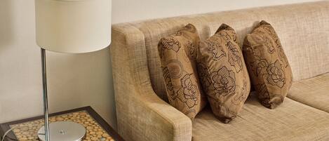 Un sofá beige con tres cojines estampados y una lámpara de mesa con base de vidrio y soporte metálico.