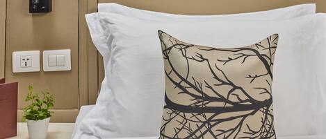 Una cama con sábanas blancas y una almohada decorativa con un diseño de rama de árbol.