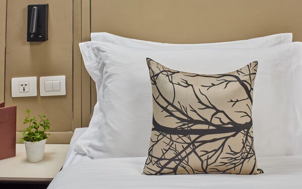 A bed with white linens and a single decorative pillow featuring a tree branch design. - Belmont Hotel Manila near NAIA Terminal 3 MNL (Pasay)